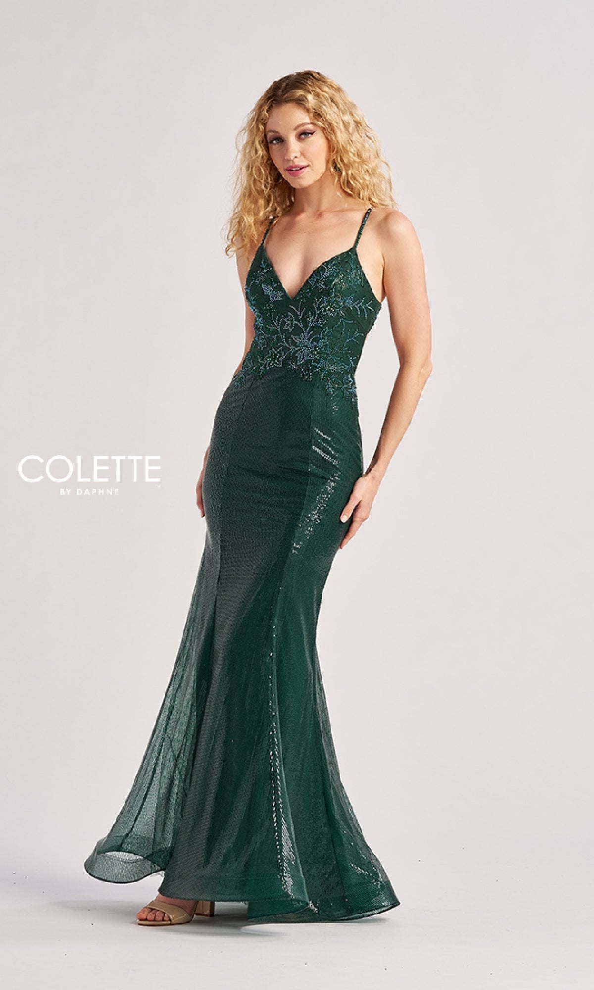 A woman in the Colette CL8585 long prom dress stands against a plain background. The dark green gown features thin straps, sequin detailing, an open back, and floor-length elegance.